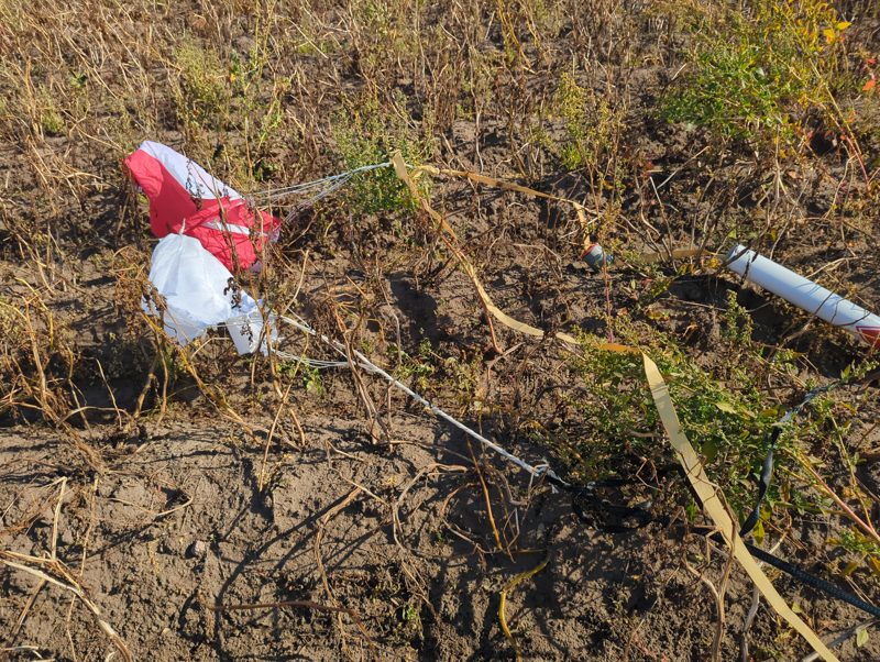 The red and white main chute and the white drogue in the field